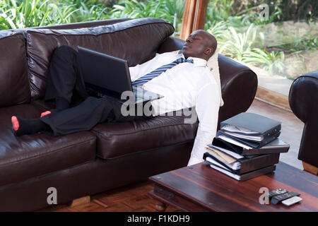 Youn African business man addormentato sul suo lettino con il suo computer portatile in appoggio sul suo giro Foto Stock