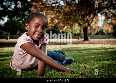 Giovane ragazza africana si trova in un parco, sorridente in telecamera Foto Stock