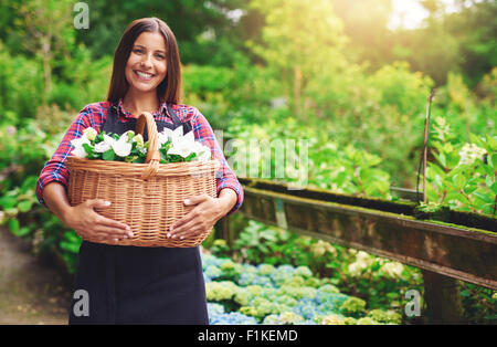 Giovane donna fioraio lavorando all'aperto presso il vivaio Fiori di raccolta in un grande cesto di vimini lei tiene nelle sue mani stand Foto Stock
