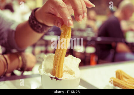 Primo piano di una donna spagnola di ammollo churros in un cioccolato Suizo, una cioccolata calda la torta con panna montata, in un caffè Foto Stock