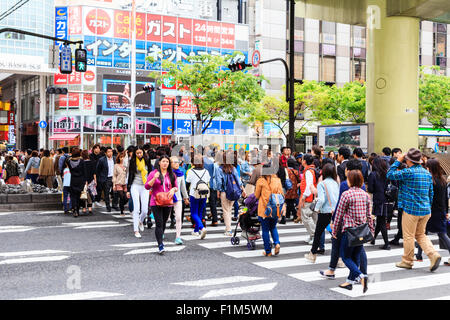 Giappone, Osaka, Dotonbori. Occupato la scena di una folla di gente che a piedi attraverso un passaggio pedonale sulla trafficata strada principale sotto un'altra strada di overhead. Foto Stock