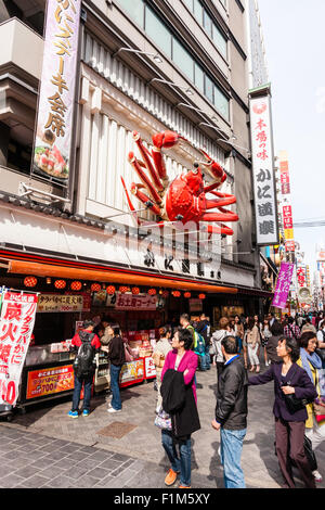 Osaka, Dotonbori. Esterno del famoso ristorante di granchio, Kani Doraku, con meccanica gigante di granchio arancione al di sopra di entrata. Strada frequentata da persone a piedi. Foto Stock
