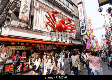 Osaka, Dotonbori. Esterno del famoso ristorante di granchio, Kani Doraku, con meccanica gigante di granchio arancione al di sopra di entrata. Strada frequentata da persone a piedi. Foto Stock