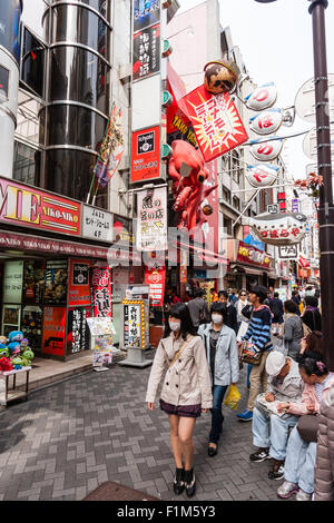 Giappone, Osaka. Dotonbori. Le persone al di fuori Takoyaki ristorante, Dotonbori Honten Kukuru, con grandi red octopus segno sopra take away finestra. Foto Stock