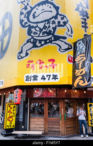 Giappone, Osaka. Dotonbori. Esterno del ramen ristorante con un grande personaggio dei fumetti di epoca Edo shop lavoratore sulla parete sopra l'entrata. Foto Stock