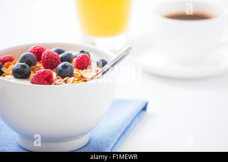 Una sana colazione con muesli, frutti di bosco freschi, succo d'arancia e una tazza di caffè. Profondità di campo, concentrarsi su bacche e m Foto Stock