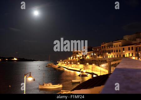 Vista attraverso il dock sotto il chiaro di luna in Menorca con barche e case in background Foto Stock