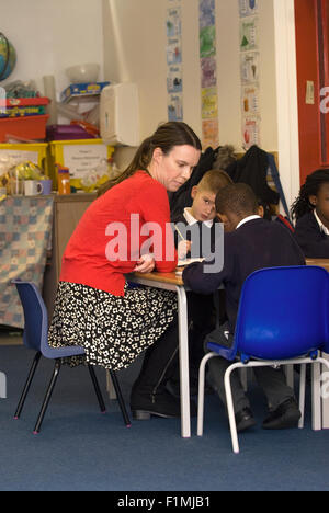 Femmina di insegnante di scuola primaria seduta con pupilla in aula, Londra, Regno Unito. Foto Stock