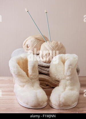 Coppia di caldo inverno pantofole di pelle di pecora (alpaca), filati di lana, ago da cucito su una pila di calda panni di lana (messa a fuoco selettiva) Foto Stock