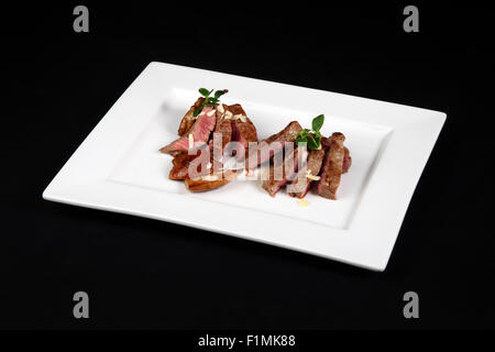 Carne di manzo con funghi in piastra bianca su sfondo nero Foto Stock