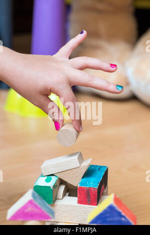 Close-up di un po' la mano della bambina a costruire qualcosa utilizzando legno pezzi geometrici, nella sua sala da gioco. Foto Stock