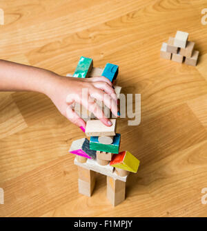 Vista superiore di un po' la mano della bambina a costruire qualcosa utilizzando legno pezzi geometrici, nella sua sala da gioco. Foto Stock