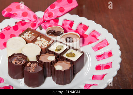 Una varietà di artigiano tartufi di cioccolato visualizzati su una piastra bianca con un nastro rosa. Foto Stock