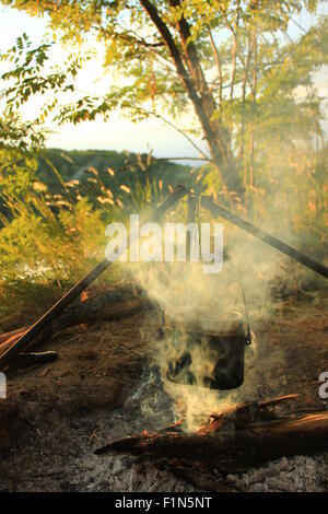 La cottura di mangiare in bowler sul fuoco in una escursione. Estate Foto Stock
