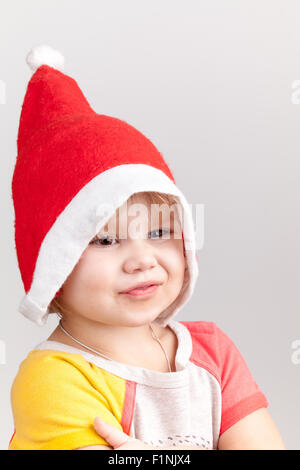 Carino caucasico sorridente bambina in rosso Santa hat su sfondo grigio, closeup ritratto in studio Foto Stock