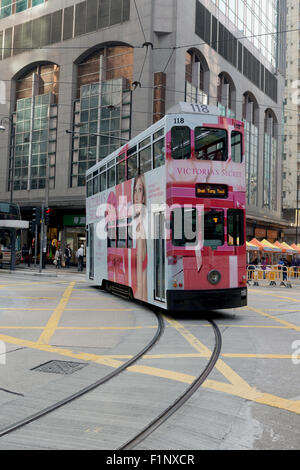 Iconico Hong Kong HK tram. Il tram su una curva stretta dando prospettiva angolata. Passando al di sopra di un giallo sezione griglia sulla strada. Foto Stock