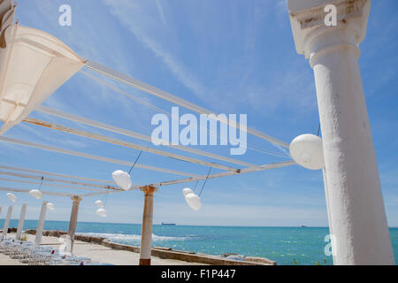 Terrazza accanto al mare con pergola, colonne e lampade di carta una giornata di vento Foto Stock