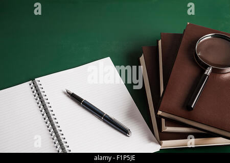 Notebook, penna stilografica e i libri di scuola sulla lavagna verde sullo sfondo Foto Stock