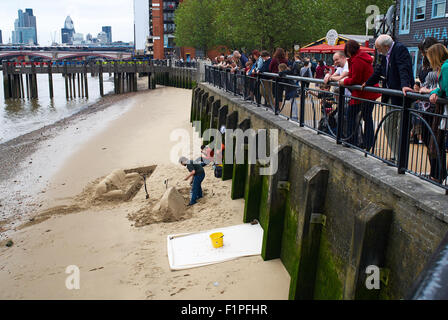 I turisti di guardare un castello di sabbia (lettino) essendo costruito sul Fiume Tamigi a Londra, Inghilterra Foto Stock