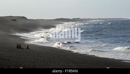 Il vento soffia e persone sedersi sulla spiaggia di ciottoli guardando le onde. Weybourne spiaggia e scogliere. Costa North Norfolk. Eng Foto Stock