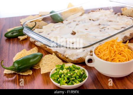 Preparazione di fagiolo stratificata dip con jalapenos, la panna acida e il formaggio cheddar Foto Stock