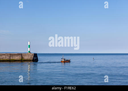 Seascape di una barca da pesca di lasciare il porto di uno stand up paddle surfer attraversa il suo percorso su un luminoso calmo mattino a Aberystwyth Foto Stock