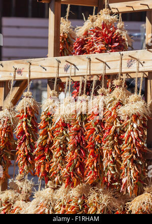 Gruppi di piccole colorate il peperoncino appeso su stringhe nel sole sono in vendita in un mercato aperto in Nuovo Messico. Foto Stock