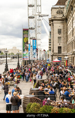 I turisti sedersi e mangiare in un bar a lato del fiume Tamigi prima di correre sulla London Eye nell estate del 2015 nel mese di agosto Foto Stock