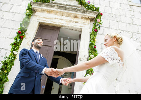 Sposa e lo sposo tenendo le mani nella parte anteriore della cappella Foto Stock