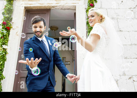 Sposa e lo sposo a giocare con le bolle di sapone di fronte cappella Foto Stock