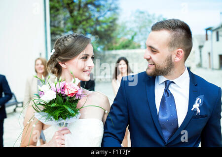 Bride and groom walking with wedding guests in background Foto Stock