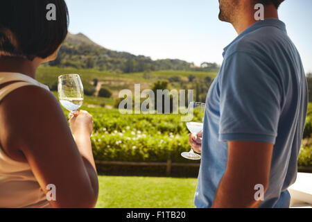 Matura in piedi insieme azienda bicchieri di vino bianco con vigneto in background. L uomo e la donna in piedi all'aperto di bere win Foto Stock