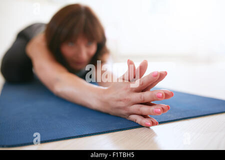 Donna facendo stretching allenamento sul tappetino fitness con le sue mani giunte. Montare femmina facendo yoga sul tappeto di esercizio in palestra. Focus su han Foto Stock