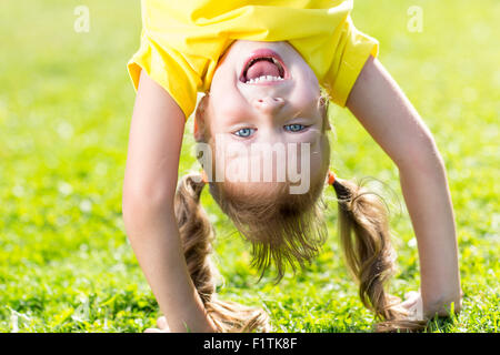 Happy child ha divertimento in piedi a testa in giù su erba verde Foto Stock