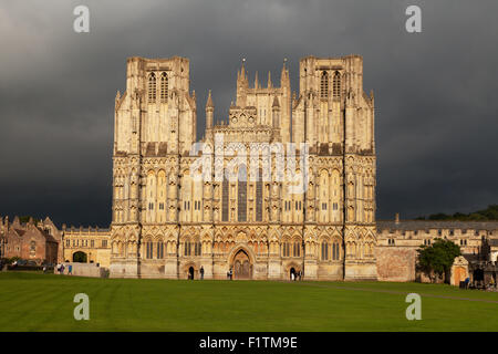 La luce solare sulla facciata ovest della Cattedrale di Wells Somerset REGNO UNITO, contro un tempestoso cielo grigio, pozzi, Somerset England Regno Unito Foto Stock