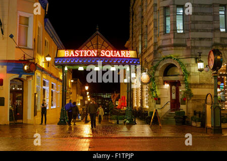 I pedoni a camminare in Bastion Square nel centro cittadino di Victoria sul bagnato di pioggia di notte-Victoria, British Columbia, Canada. Foto Stock