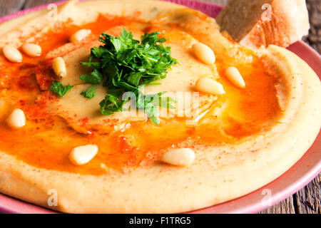 Hummus con prezzemolo, pinoli sulla piastra e rustico sfondo di legno vicino fino Foto Stock