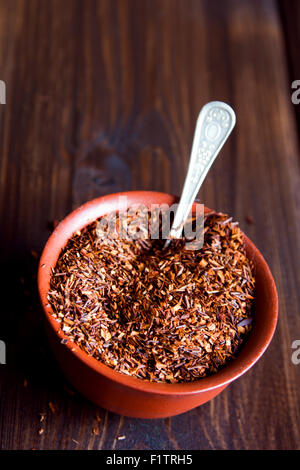 Essiccato rooibos tè nel recipiente di ceramica su sfondo in legno, luce naturale Foto Stock