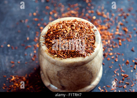 Essiccato rooibos tè nel recipiente di pietra nera su sfondo di metallo, luce naturale Foto Stock