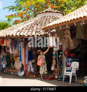 La donna che acquista ispeziona gli articoli per la vendita nel negozio sull'isola del fiume Cuale, un luogo vivace di incontro e mercato, Puerto Vallarta, Messico. N. 613 PV Foto Stock