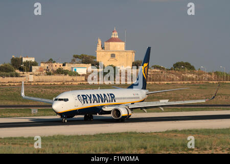 Basso costo viaggi aerei nell'Unione europea. Ryanair Boeing 737-800 jet piano in arrivo in Malta, con Ta' Loretu cappella, Gugja, fornendo una cornice mediterranea Foto Stock