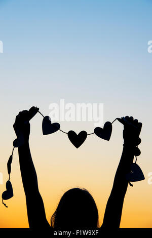 Ragazze mani cuori su una stringa al tramonto. Silhouette Foto Stock