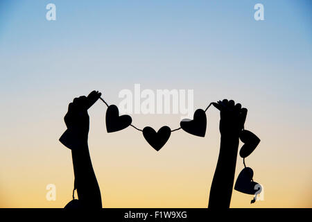 Ragazze mani cuori su una stringa al tramonto. Silhouette Foto Stock