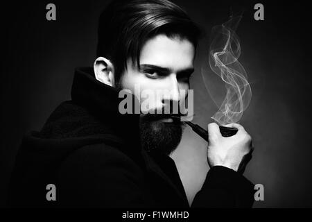 Dark artistico ritratto del giovane bella l'uomo. Il giovane uomo fuma un tubo. Close up. Foto in bianco e nero Foto Stock