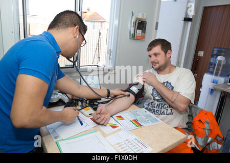 Lavoratori edili tenendo del Test della pressione del sangue e lo stato di salute generale controllare sul sito, England, Regno Unito Foto Stock