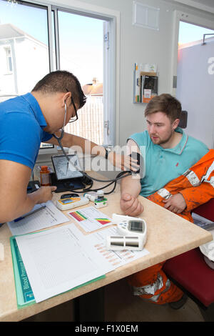 Lavoratori edili tenendo del test della pressione del sangue e lo stato di salute generale controllare sul sito, England, Regno Unito Foto Stock