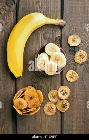 Le banane fresche e i chip sul tavolo di legno, vista dall'alto. Focus sui prodotti freschi fette di banane Foto Stock