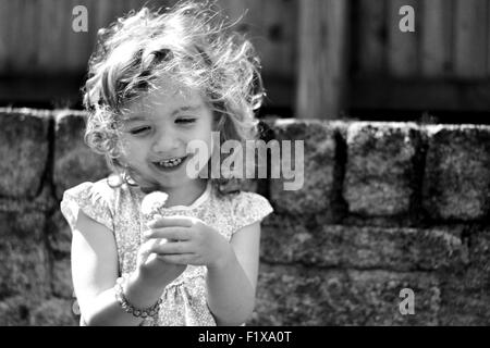 Bambina contiene un orologio di tarassaco e risate Foto Stock