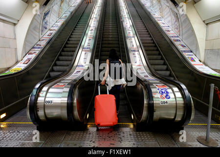 Vista posteriore di una persona con un rosso valigia scorrevole salendo su una scala mobile Foto Stock