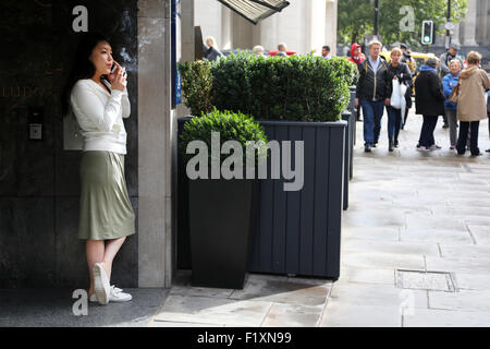 Londra 2015: un lavoratore di ufficio prende una pausa sigaretta al di fuori del suo ufficio edificio quali fronti su una strada trafficata. Lei con il suo mobile Foto Stock